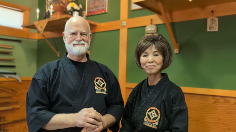 Stephen K. Hayes and Rumiko Urata Hayes wearing black martial arts uniforms in their home dojo, the To-Shin Do Hombu.